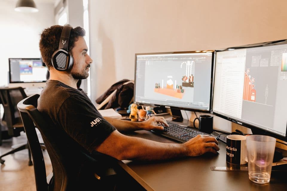 An artist at a desk working on 3D scenes across two monitors